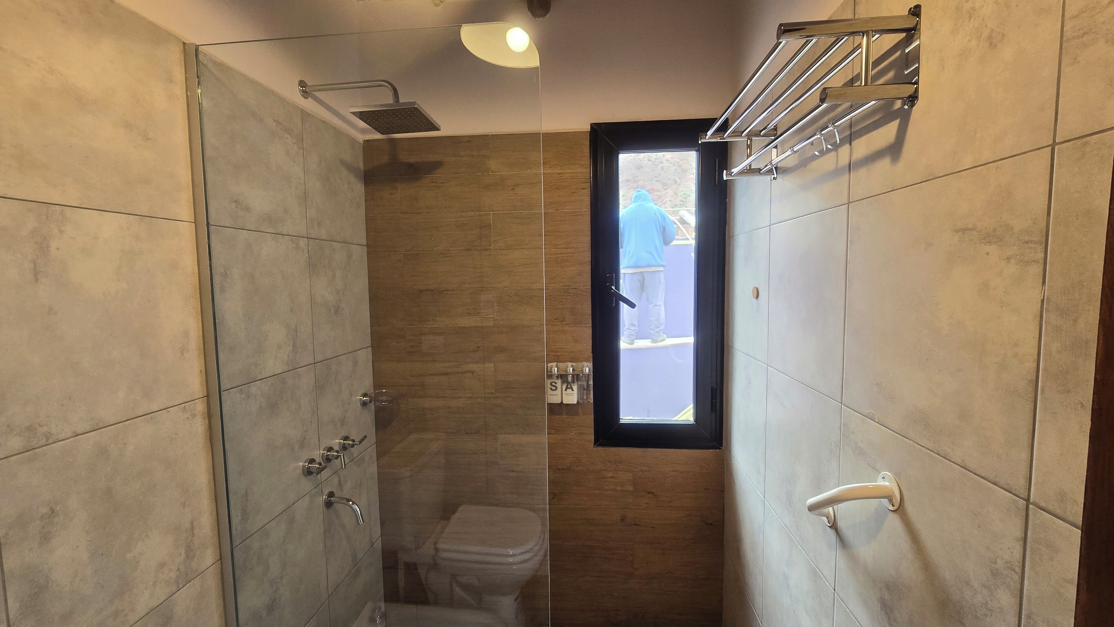 A modern bathroom with a shower, toilet, and a window providing natural light.