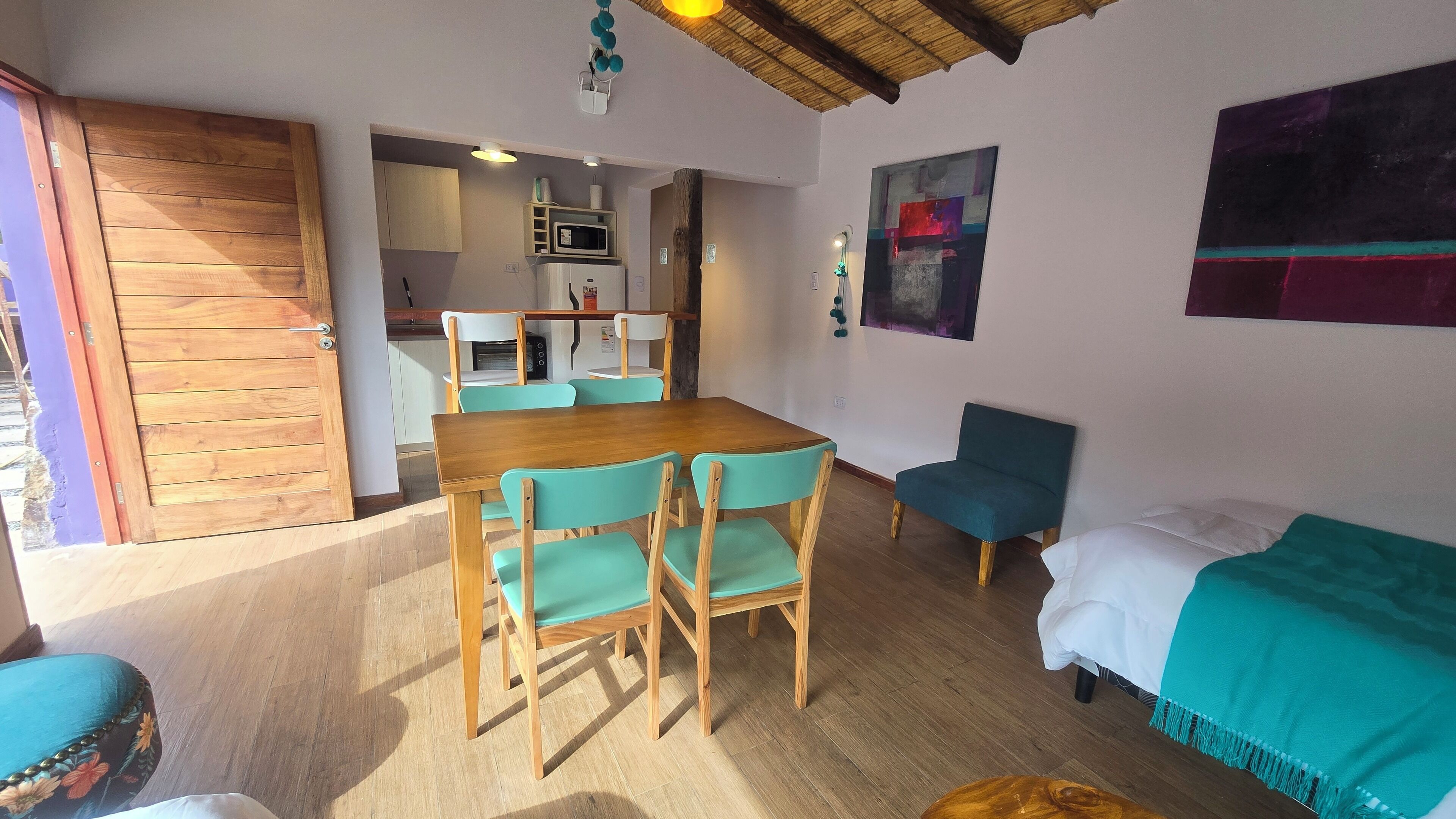 A cozy room with a wooden dining table, teal chairs, a teal sofa, and a bed with a teal cover.