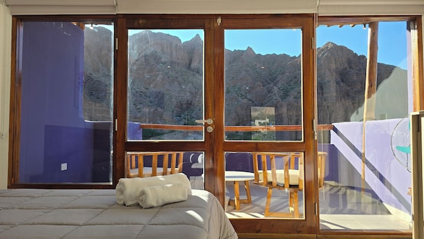 A bedroom with a bed, a balcony with a table and chairs, and a view of mountains. - El cielo en Tilcara complejo turístico (Tilcara)