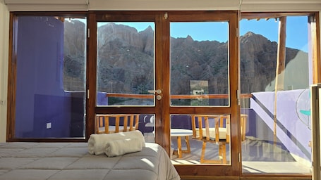 A bedroom with a bed, a balcony with a table and chairs, and a view of mountains.