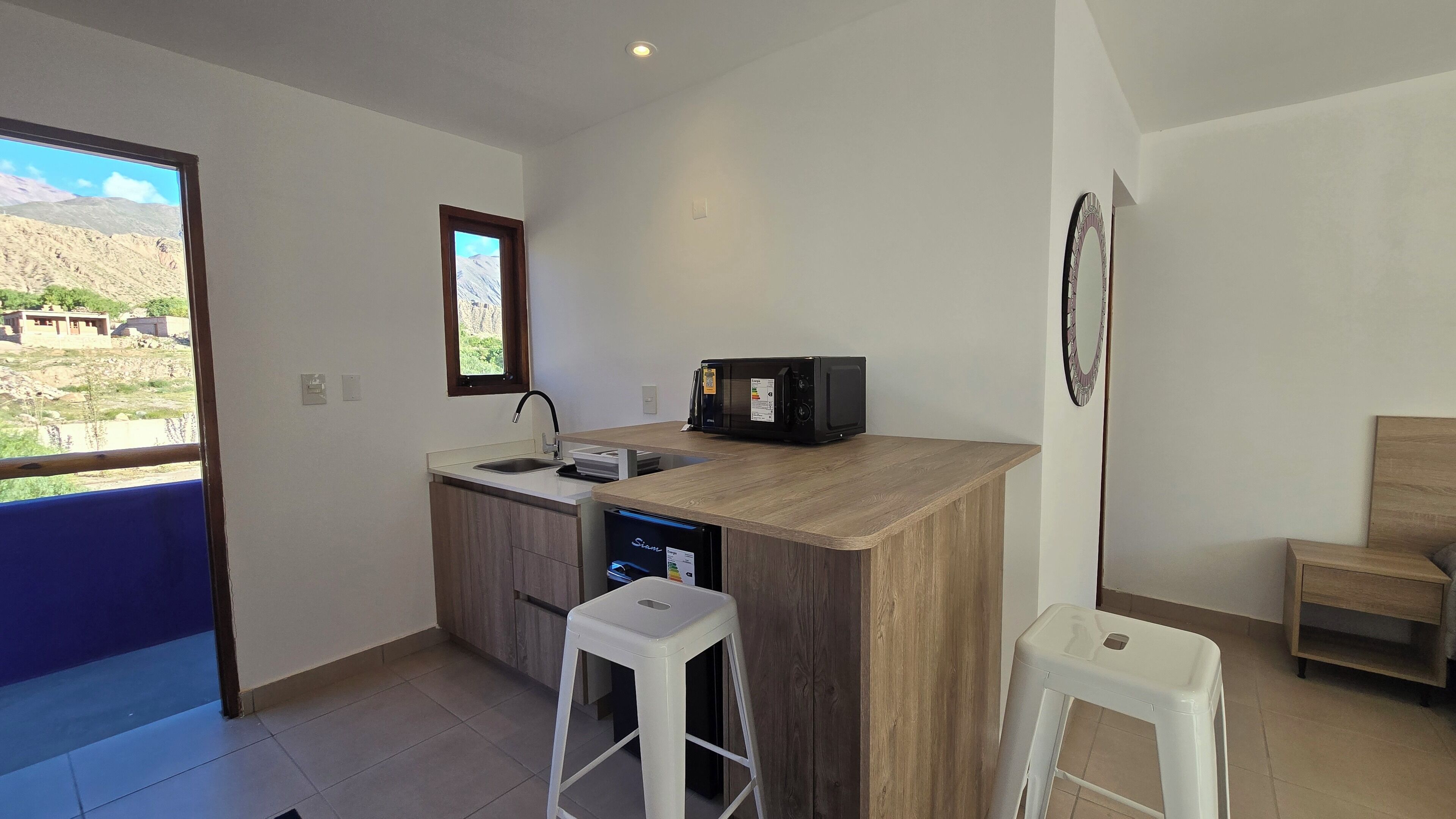 Una cocina compacta con microondas integrado, un lavamanos pequeño y una ventana con vistas a un paisaje montañoso.