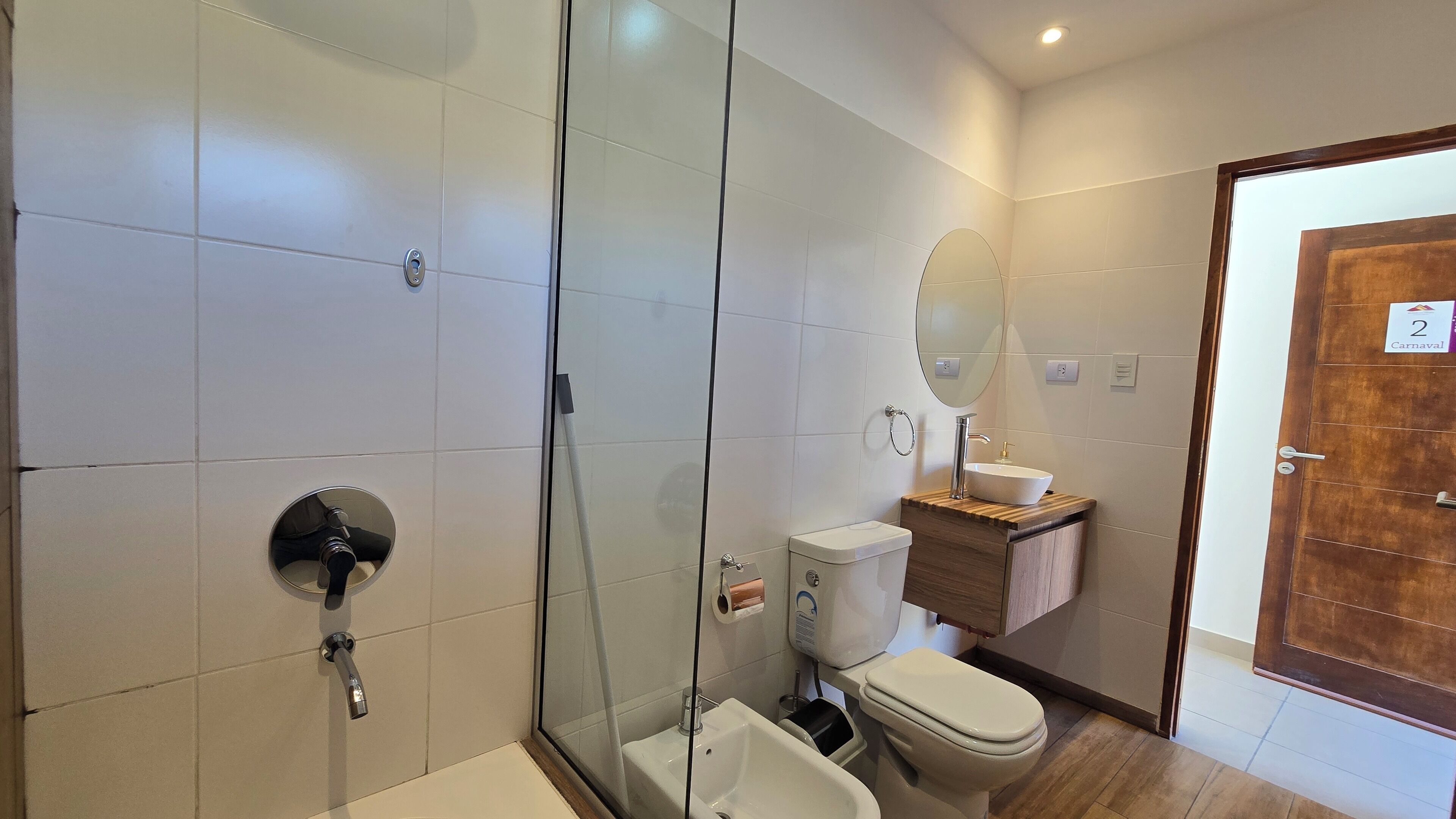 Un baño moderno con cabina de ducha de vidrio, inodoro blanco y tocador de madera con lavamanos.