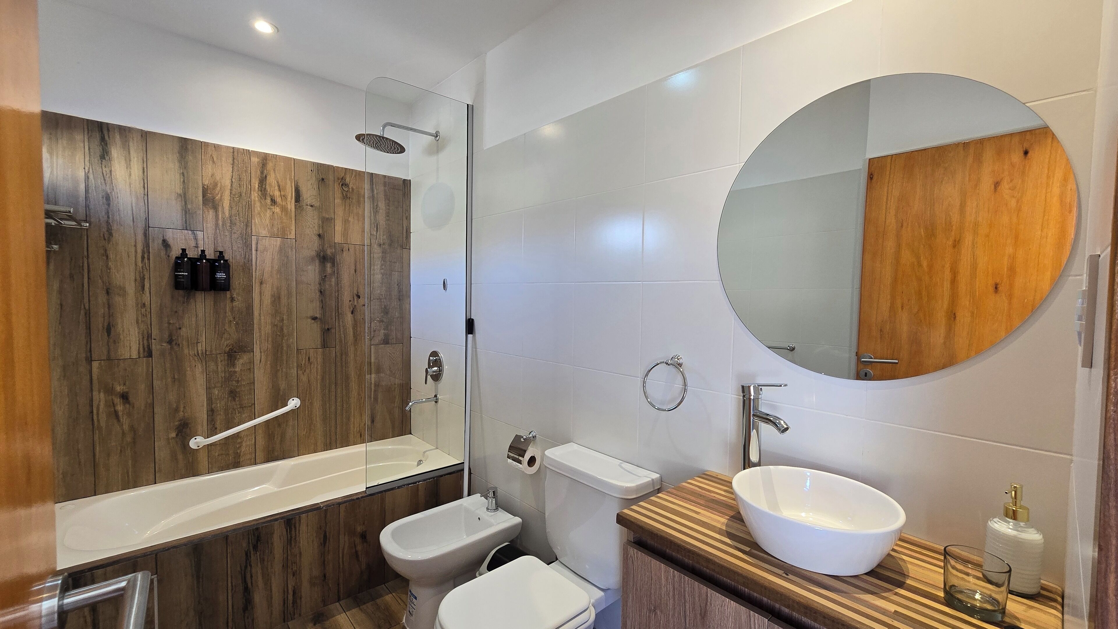 Un baño moderno con tocador de madera, bañera independiente, inodoro y un espejo grande.