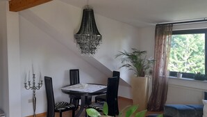 Uma sala de jantar com uma mesa redonda, cadeiras pretas, um candelabro e um vaso com planta.