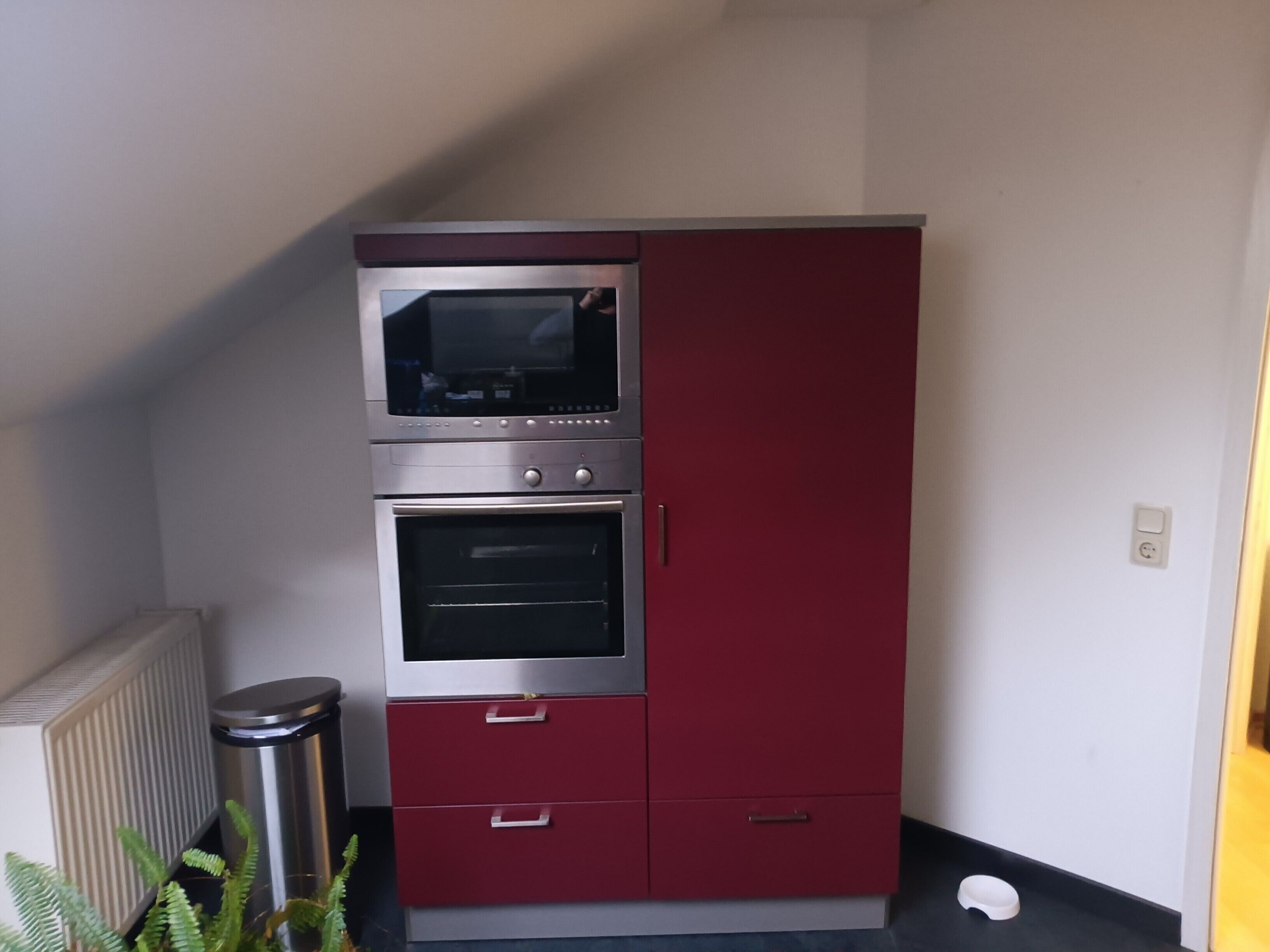 Una cucina con forno a incasso e microonde, un cestino e un termosifone.