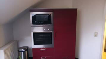 Una cucina con forno a incasso e microonde, un cestino e un termosifone.