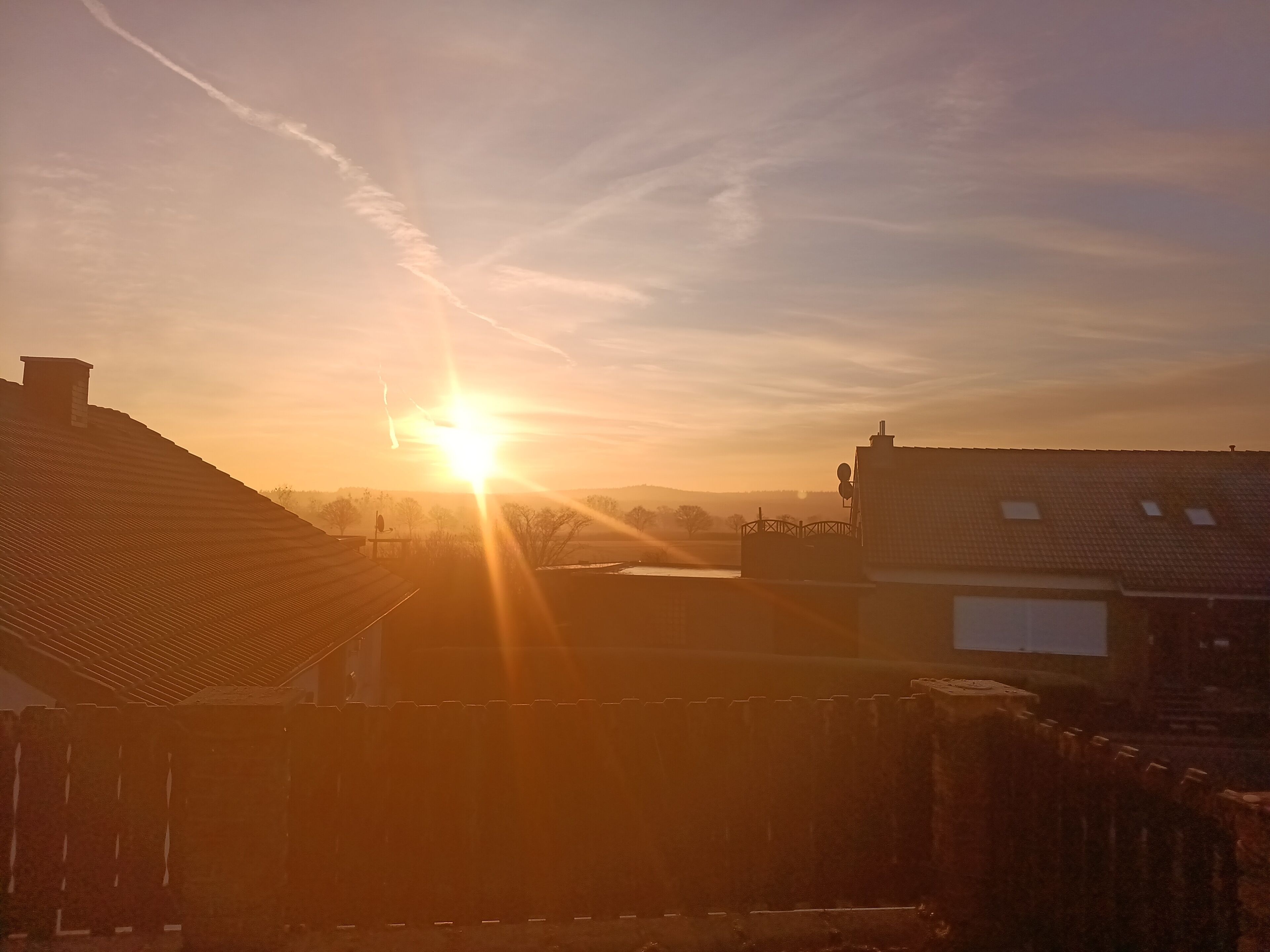 Een zonsondergang boven een woonwijk met huizen en een heldere lucht.