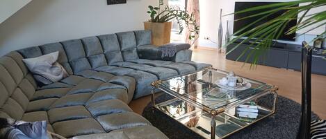 Un salon moderne avec un canapé d’angle, une table basse en verre et un grand tableau abstrait accroché au mur.