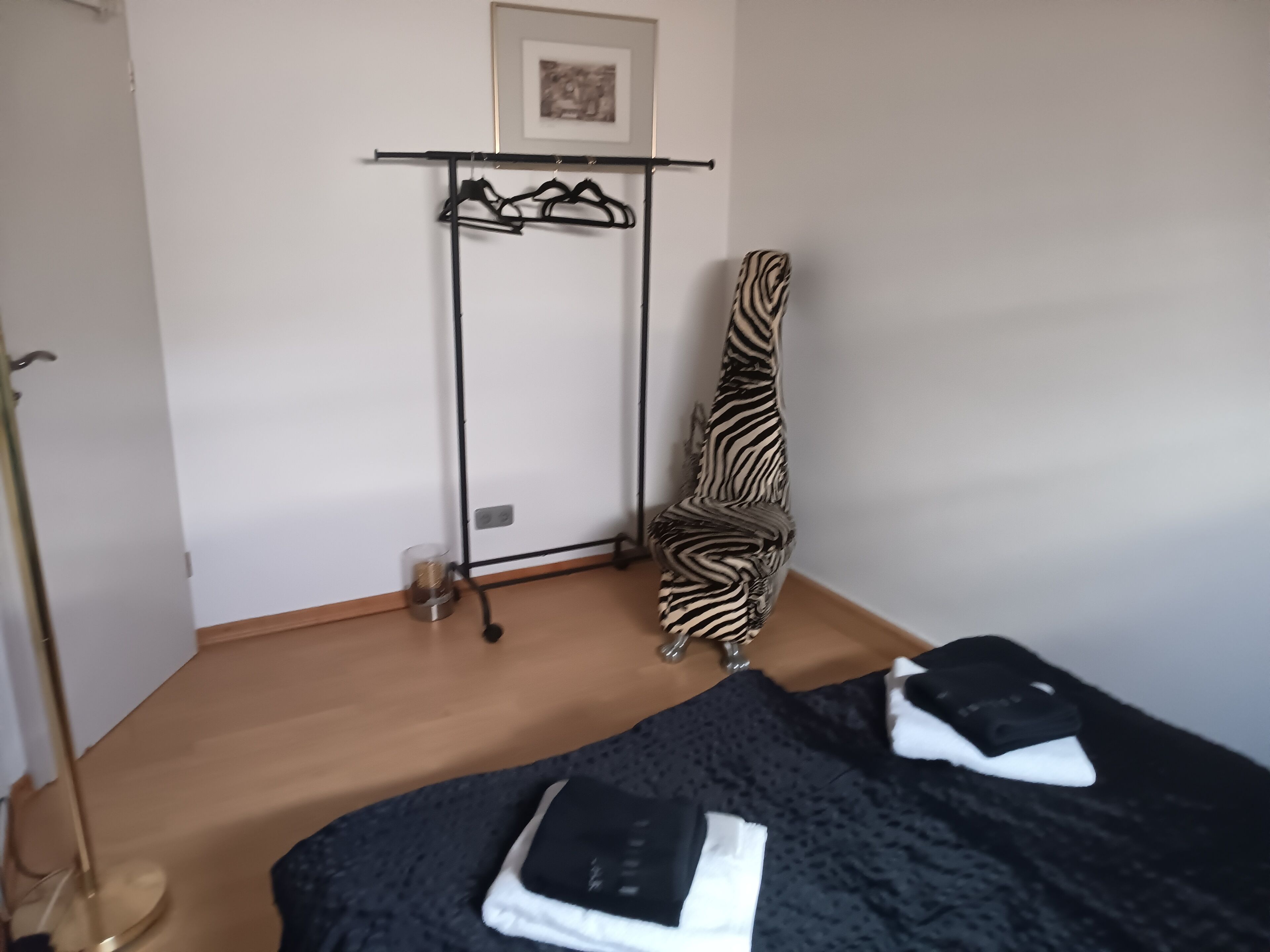 A room with a bed, a zebra-patterned chair, a coat rack, and a framed picture on the wall.
