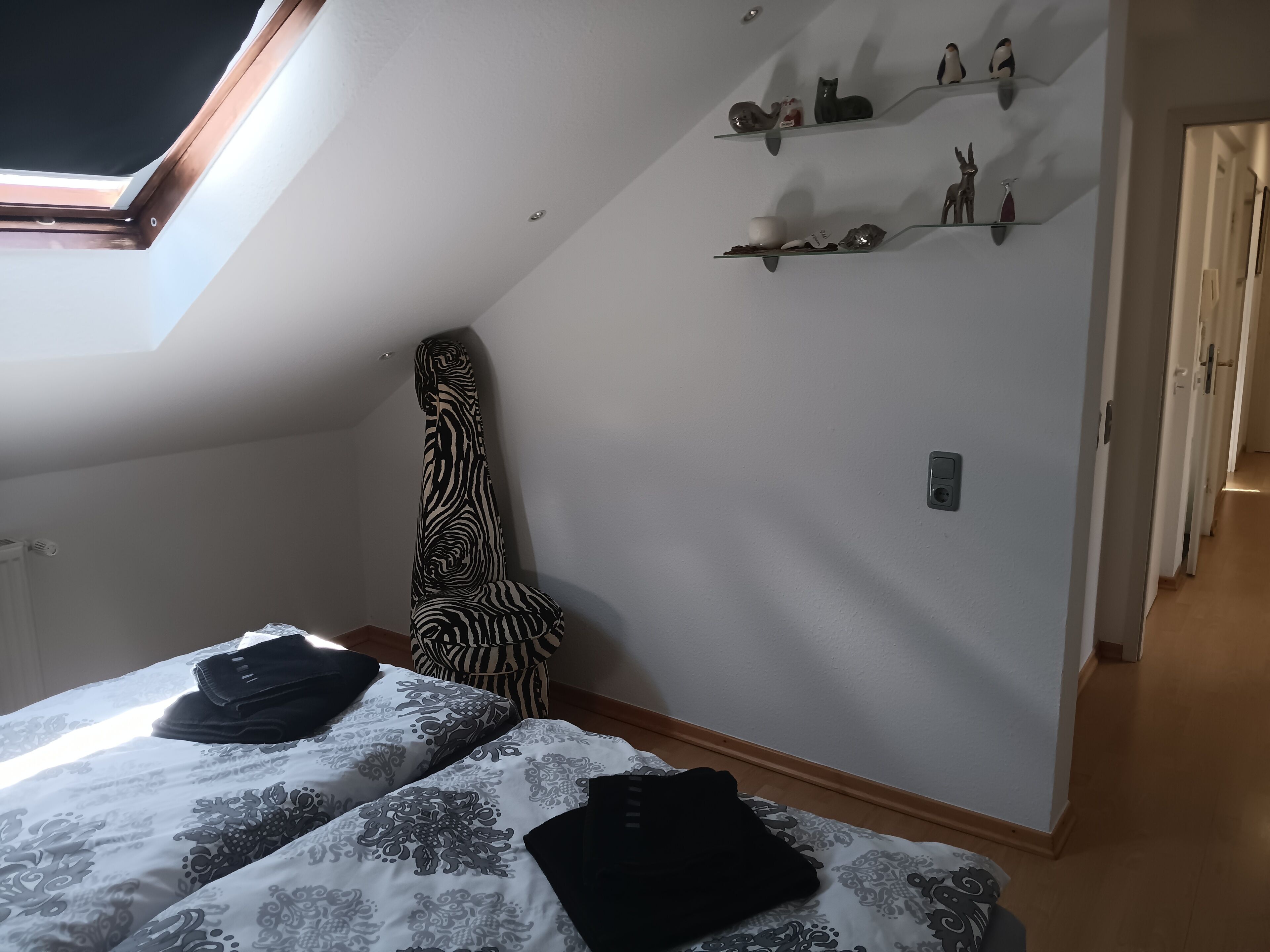 Ein Schlafzimmer mit Oberlicht, einem zebra-gemusterten Sessel, einem Bett mit gemusterten Textilien und einem Flur mit einer Tür.