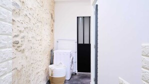 Un pasillo estrecho con una pared de ladrillo blanco a un lado y una pared blanca al otro, que conduce a una puerta con marco negro.