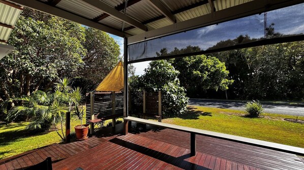 Enjoy the serene view of the lush garden from this outdoor terrace with a wooden deck and large window.
