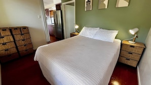 A neatly made bed with white linens in a room with green walls, a wooden floor, and a small bedside table with a lamp. - Rainbow North - Rainbow Beach (Rainbow Beach)