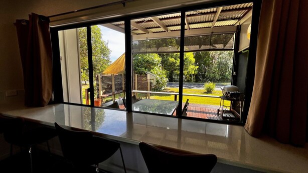 A room with a large window overlooking a garden and outdoor seating area. - Rainbow North - Rainbow Beach (Rainbow Beach)