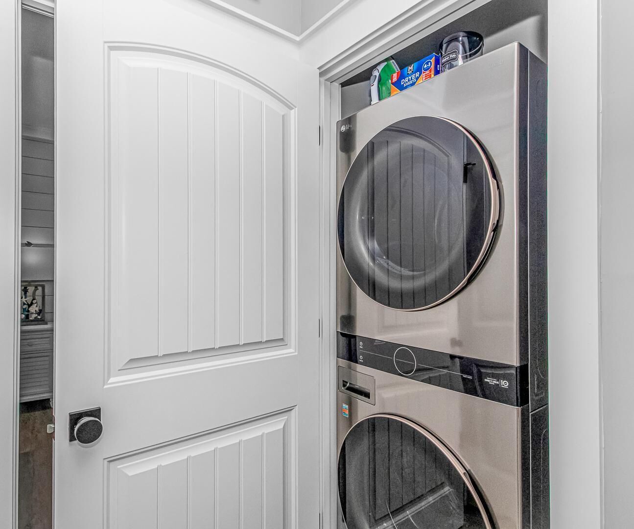 A laundry room with two stacked washers and dryers, a white door, and a shelf with laundry supplies.