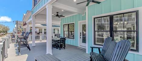 A covered outdoor deck with a table and chairs, a ceiling fan, and a view of the ocean.