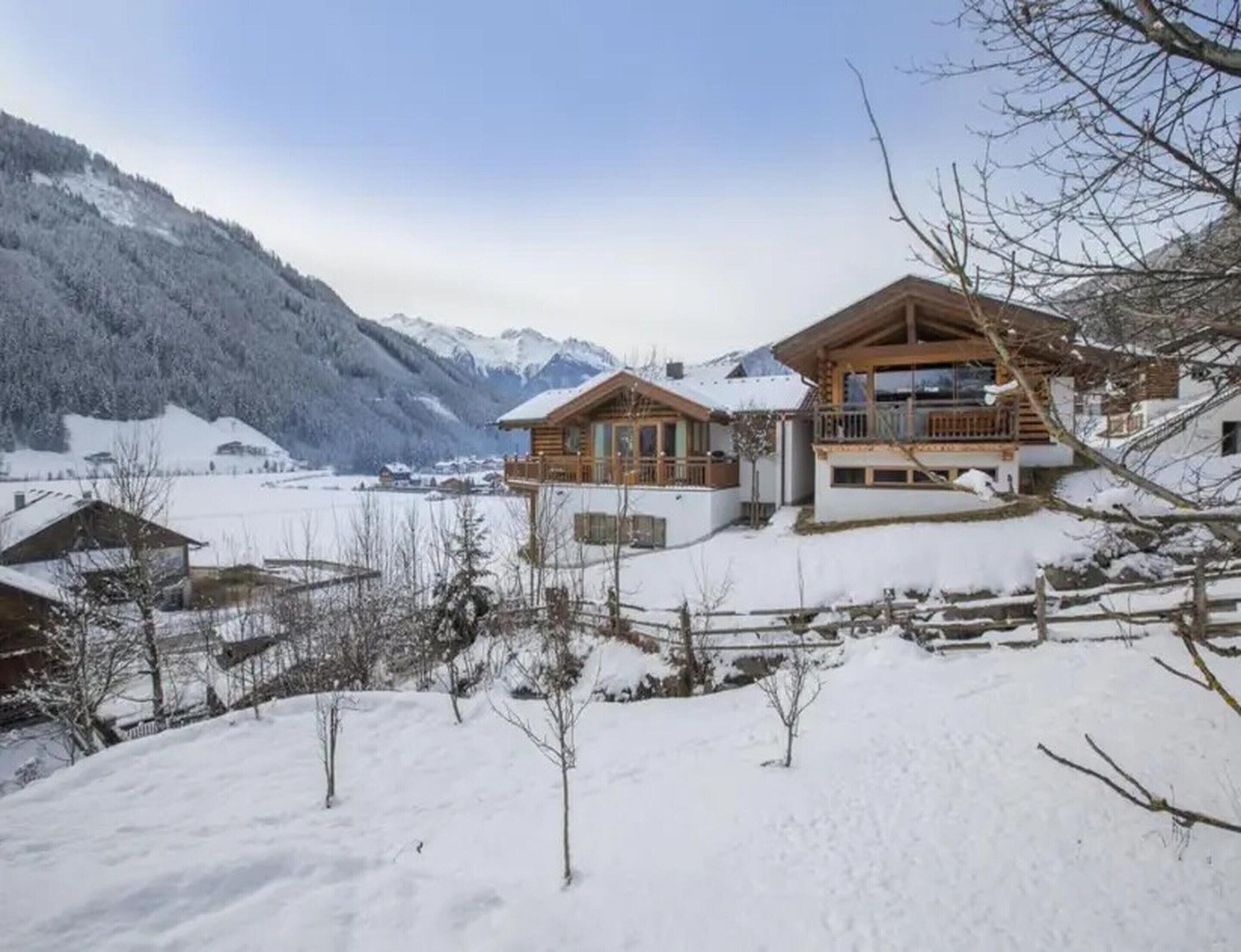 Un chalet en bois doté d’un balcon, entouré de montagnes enneigées et surplombant un ciel dégagé.