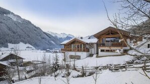 Un chalet in legno con un balcone, immerso in montagne innevate e un cielo sereno.