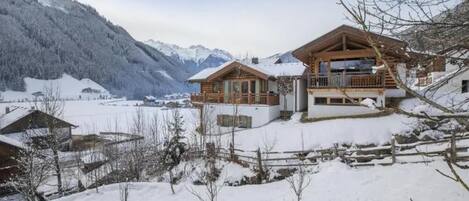 Un chalet en bois doté d’un balcon, entouré de montagnes enneigées et surplombant un ciel dégagé.