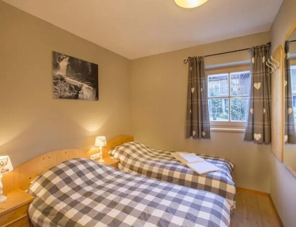 Un dormitorio con dos camas, una mesita de noche, una lámpara, una ventana con cortinas y un cuadro en la pared.