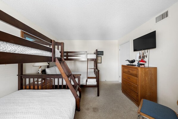 Een slaapkamer met een stapelbed, een houten dressoir, een bureau en een televisie aan de muur.