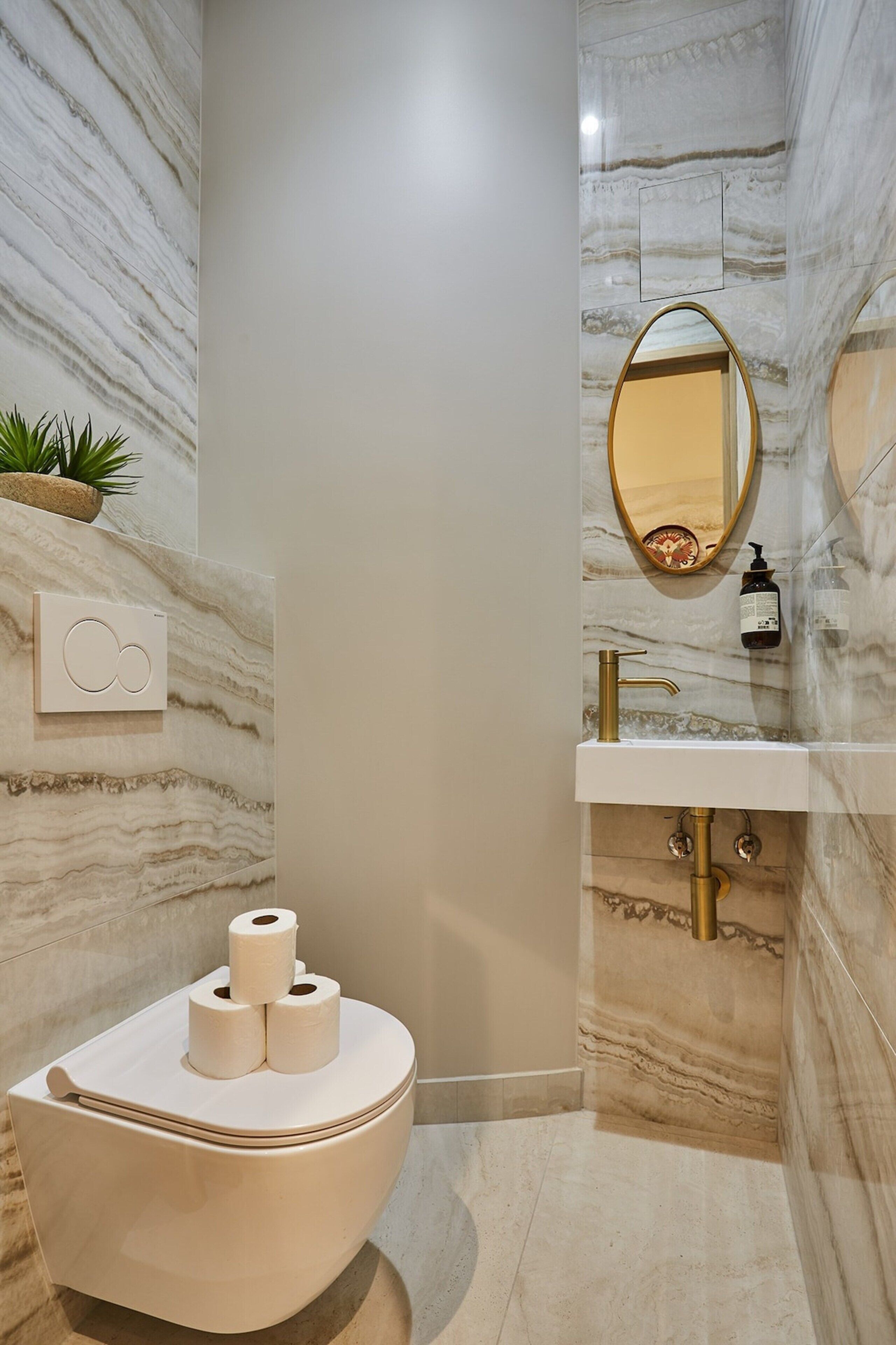 Ein Badezimmer mit Marmorwand, freistehender Toilette, Waschbecken mit Goldarmatur und Spiegel mit goldfarbenem Rahmen.