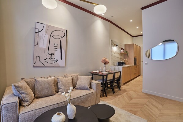 Uma sala de estar moderna com sofá, mesa de centro e obras de arte. Uma área de refeições com mesa e cadeiras é visível ao fundo.