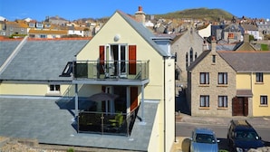 Un immeuble de deux étages doté d’un balcon, offrant une vue dégagée sur la rue en contrebas et sur une colline en arrière-plan.