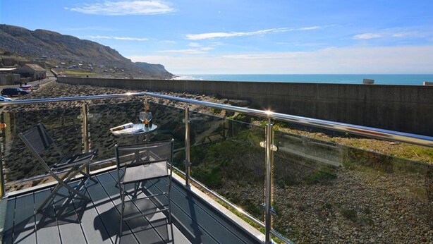 Un balcon doté d’une balustrade en verre, offrant une vue sur une plage rocheuse et l’océan.