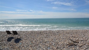 Une plage de galets avec deux chaises disposées face à l’océan, sous un ciel dégagé.