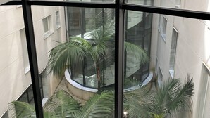 Un atrio moderno con techo de vidrio que ofrece vistas a un patio con palmeras y una fuente central.