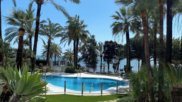Zona de piscina con palmeras, un sendero de piedra y vista despejada al océano.