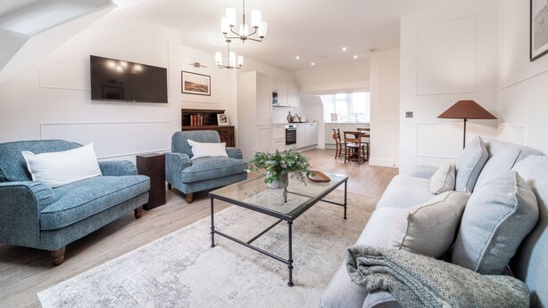 Ein geräumiges Wohnzimmer mit einem Glastisch, zwei Sofas, einem Fernseher und einer Chandelier.