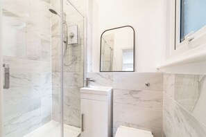 Ein modernes Badezimmer mit einer Duschkabine aus Glas, einem weißen Waschbecken und einer Wand mit Marmorplatten.
