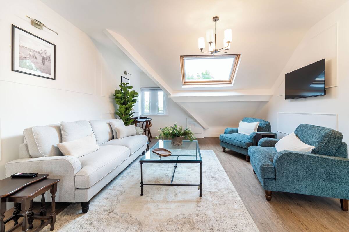 Un salon moderne avec un canapé blanc, un fauteuil bleu, une table basse en verre et un téléviseur fixé au mur.