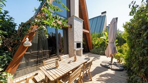 A wooden deck with a table and chairs, a stone fireplace, and a pergola with climbing plants. - BEGONVİL GÜMÜŞLÜK  (Bodrum)
