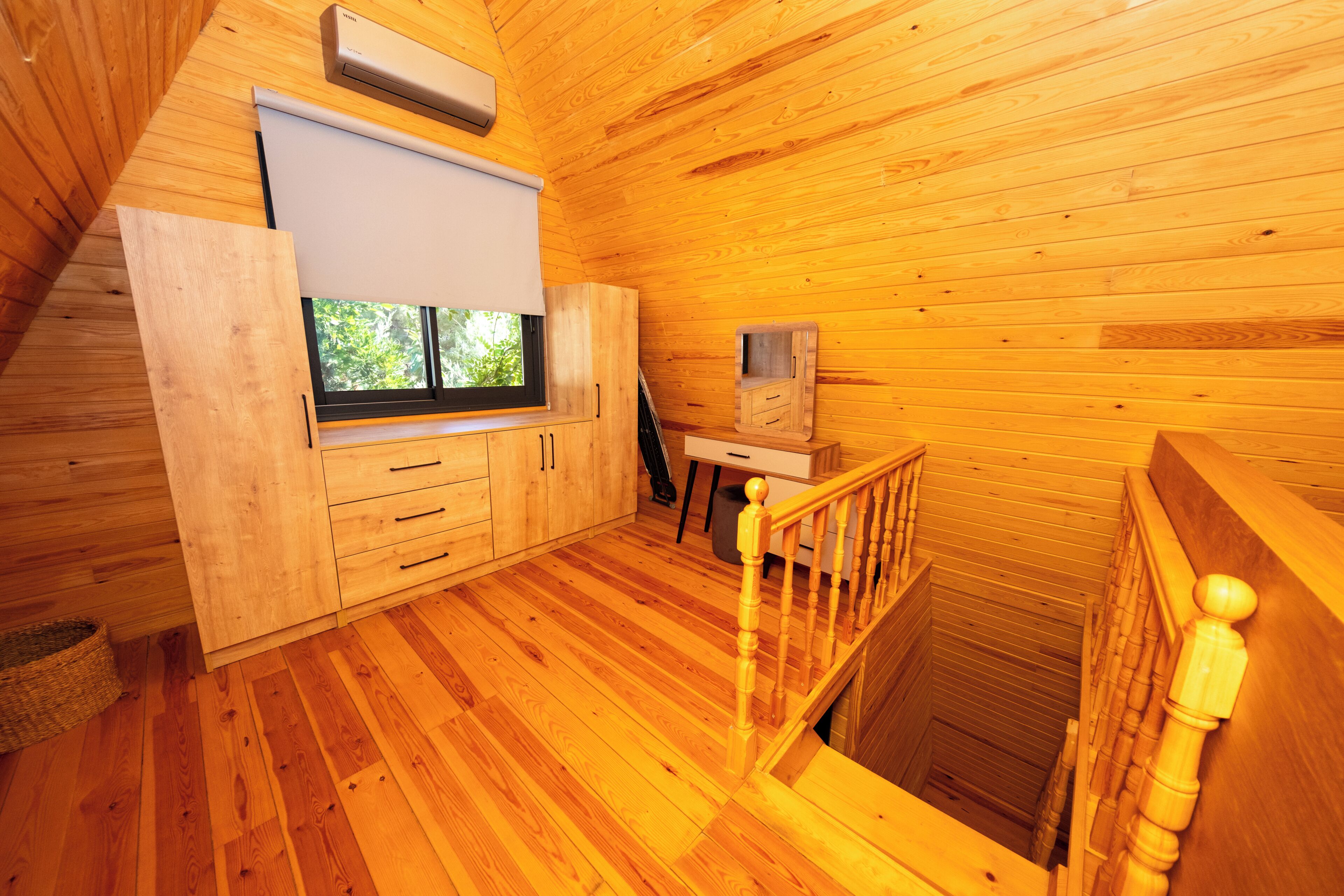 A wooden cabin interior with a window, wooden staircase, and a small desk area.