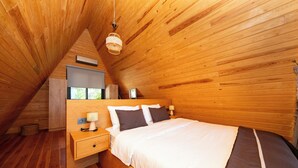 A bedroom with a wooden ceiling, a bed with white and brown bedding, a nightstand with a lamp, and a window. - BEGONVİL GÜMÜŞLÜK  (Bodrum)