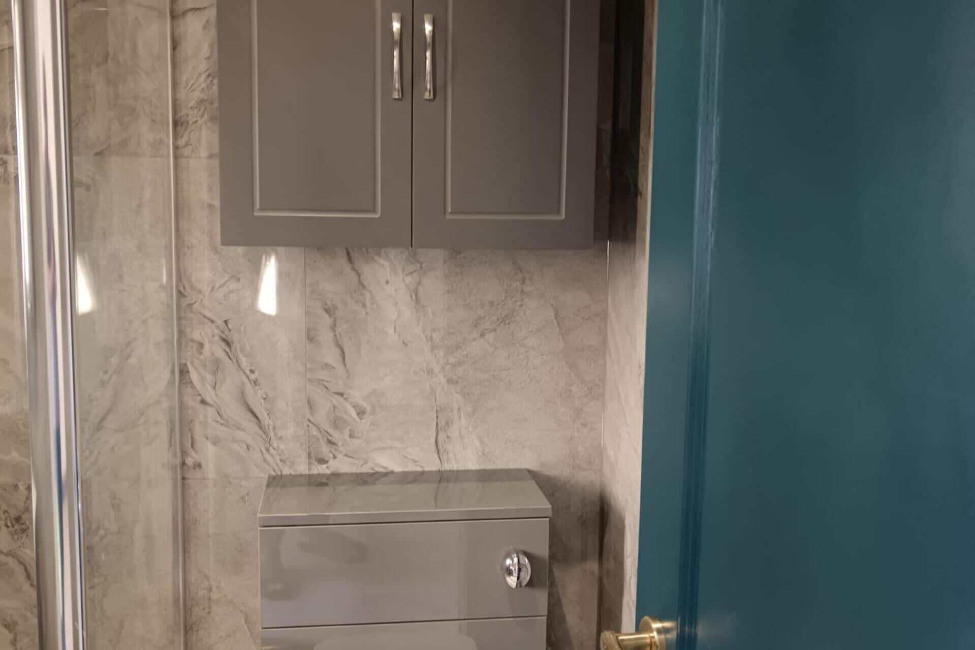 Un baño con pared de mármol, un mueble con dos puertas y una puerta azul.