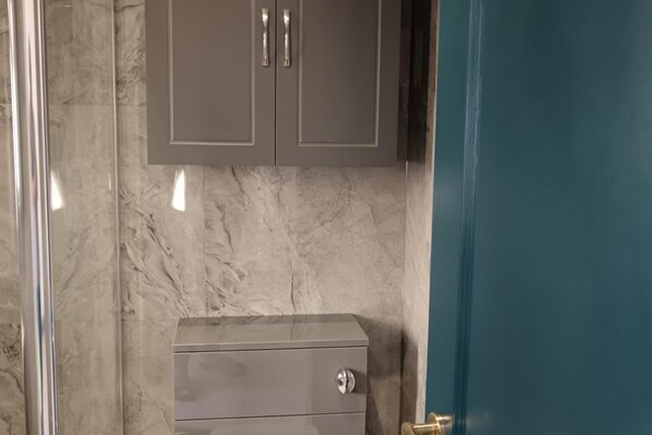 A bathroom with a marble wall, a cabinet with two doors, and a blue door. - High Wycombe 1-bed Apt, Sleeps 3 & Private Parking (High Wycombe)