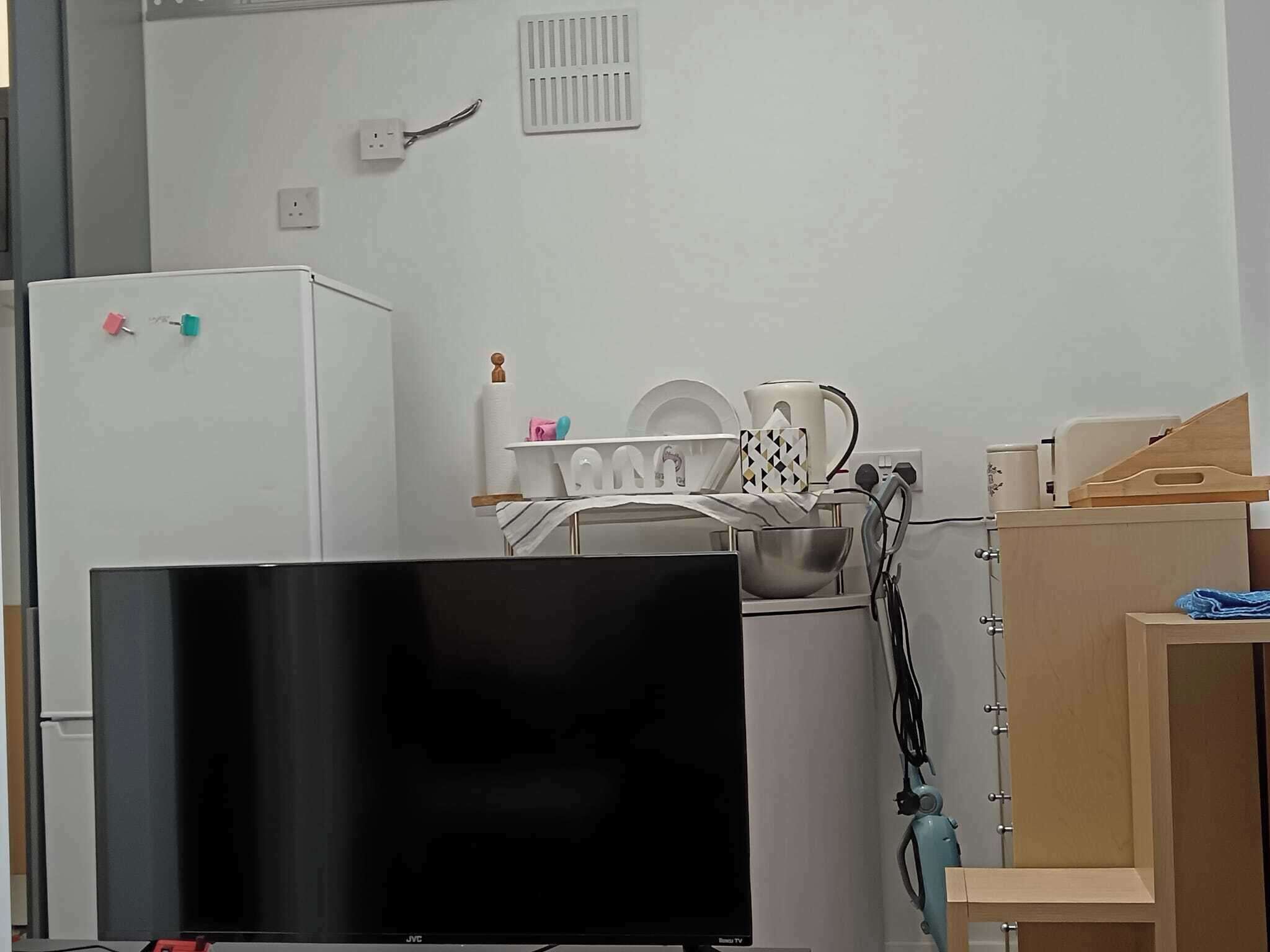 A kitchenette with a refrigerator, a TV, a dish rack, and a coffee maker.