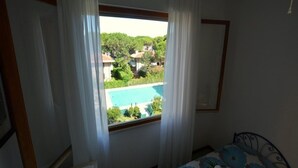 A bedroom with a view of a swimming pool and greenery outside. - Fantastic Flat With Pool View Just Steps From the sea (Lignano Sabbiadoro)