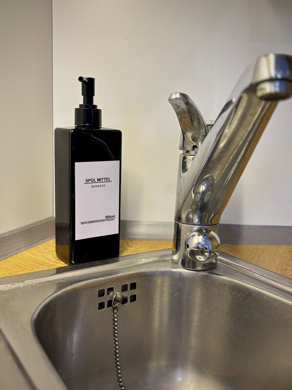 Un lavamanos de acero inoxidable con un grifo moderno y una botella de artículos de baño.