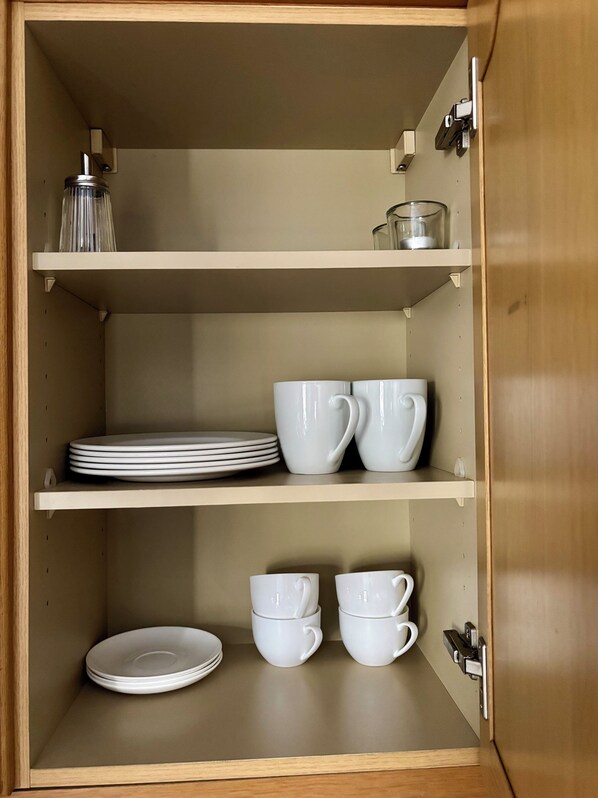 Un armario de madera con estantes que contienen platos, tazones y tazas blancos.