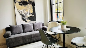 En moderne stue med en sort sofa, et rundt bord med en plante, og et stort abstrakt billede på væggen.