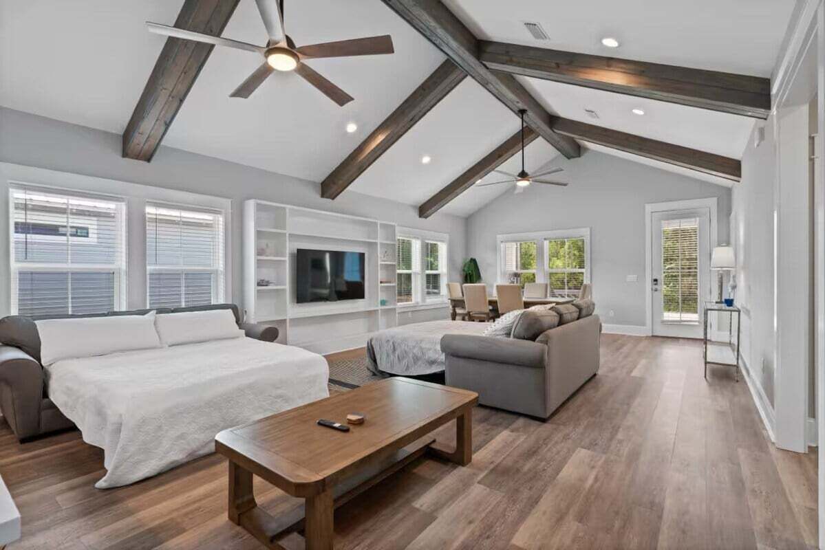 A spacious living room with a high ceiling, wooden beams, a large bed, a sofa, and a TV.