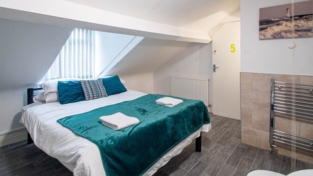 Een slaapkamer met dakraam, een bed met een blauwgroene sprei, witte kussens en een witte handdoek.