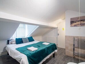 A bedroom with a skylight, a bed with a teal bedspread, white pillows, and a white towel.