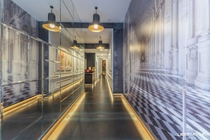 A corridor with glass walls, a checkered floor, and hanging pendant lights. - Libertad 24 (Madrid)