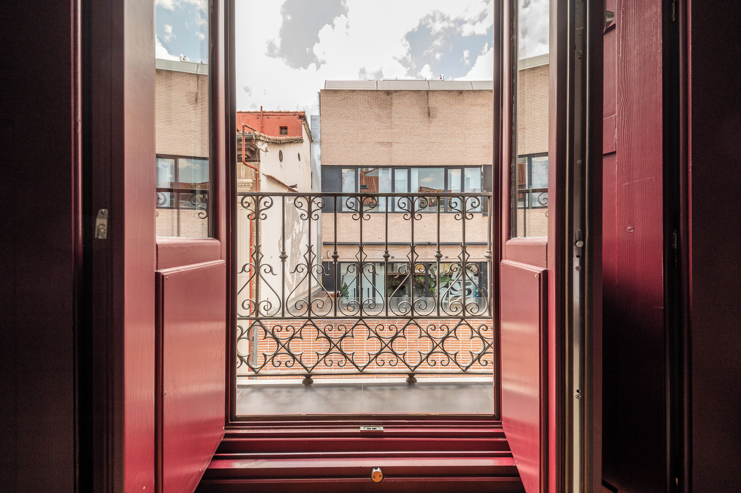 Vista desde un balcón con barandillas de hierro forjado y una puerta roja.